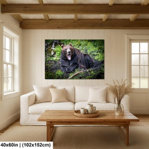 May include: A rectangular wall art print featuring a brown bear lying on green grass with yellow flowers, mouth open in a yawn. The print measures 40 by 60 inches and is displayed on a white paneled wall above a white sofa and wooden coffee table.
