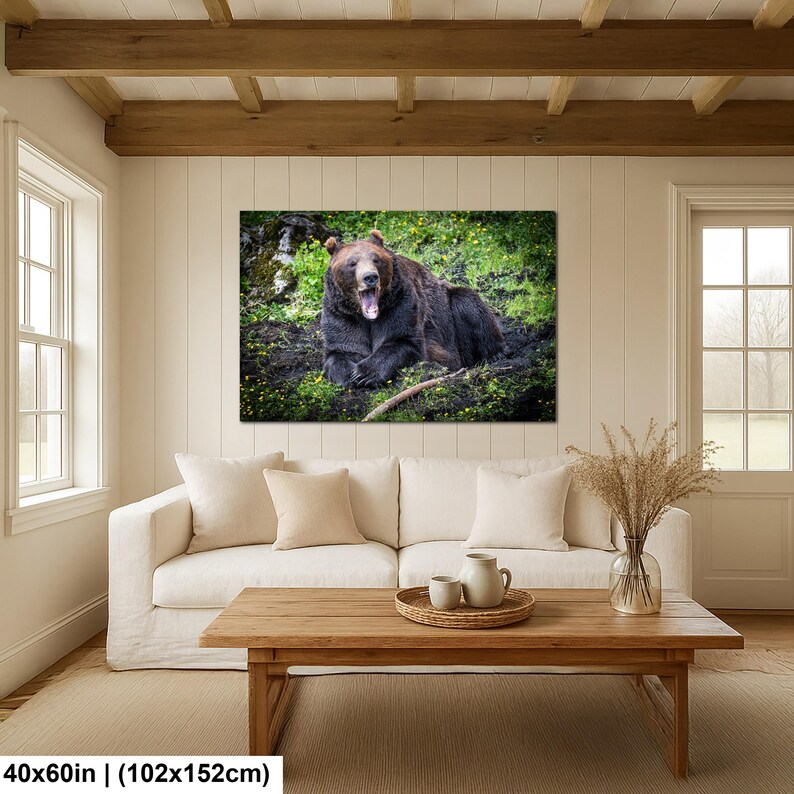 May include: A rectangular wall art print featuring a brown bear lying on green grass with yellow flowers, mouth open in a yawn. The print measures 40 by 60 inches and is displayed on a white paneled wall above a white sofa and wooden coffee table.