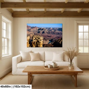 May include: A rectangular wall art print depicting a panoramic view of the Grand Canyon with layered red rock formations and a winding river below, displayed in a living room above a white sofa and a wooden coffee table, measuring 40x60 inches.