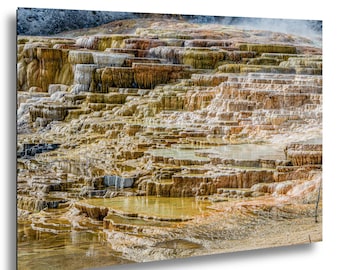 Puede incluir: Una fotografía de paisaje de Mammoth Hot Springs que muestra terrazas de travertino escalonadas con agua que fluye. Los depósitos minerales presentan tonos naranja, amarillo, marrón y blanco, creando una formación geológica en capas y escalones.