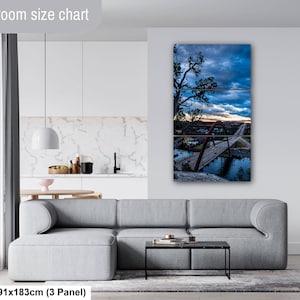 May include: A three-panel wall art set depicting a bridge over water at sunset under a cloudy blue sky. The artwork is displayed on a wall above a gray sofa. The text "Livingroom size chart" and "36x72in | 91x183cm (3 Panel)" is visible.