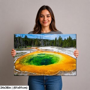 May include: A rectangular wall art print measuring 24 by 36 inches, featuring a vibrant landscape photograph of a geothermal hot spring with a deep green center surrounded by bright orange and yellow mineral deposits and a forest background.
