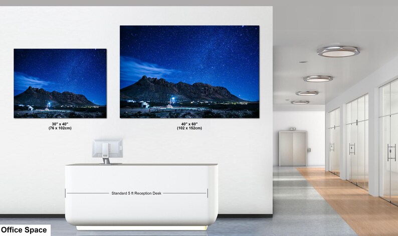 Puede incluir: Dos impresiones de arte mural rectangulares que muestran un paisaje nocturno con una cordillera bajo un cielo azul estrellado. La impresi&oacute;n peque&ntilde;a mide 76 x 102 cm y la grande 102 x 152 cm, expuestas sobre un mostrador de recepci&oacute;n de 5 pies.
