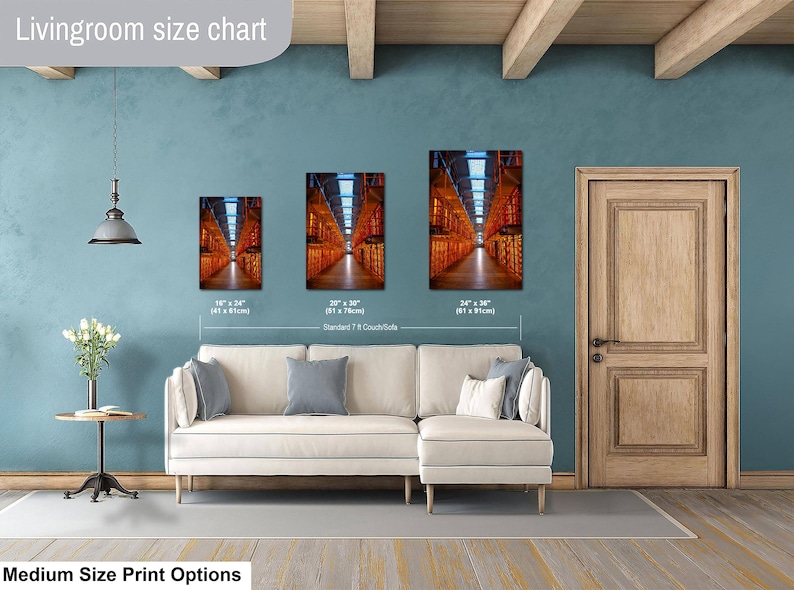 May include: A living room size chart displaying three rectangular wall art prints of a warehouse interior with orange lighting. The prints are labeled with dimensions 16" x 24", 20" x 30", and 24" x 36" above a white sectional sofa and a small side table.