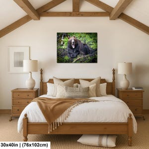 May include: A rectangular wall art print featuring a brown bear with its mouth open, resting in a green forest setting. The print measures 30 by 40 inches and is displayed above a wooden bed frame with a white duvet and a tan throw blanket.
