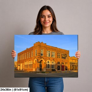 May include: A rectangular wall art print measuring 24 by 36 inches, featuring a photograph of a multi-story orange brick building with arched windows and a sign reading Depot. The structure is set against a clear blue sky during golden hour.