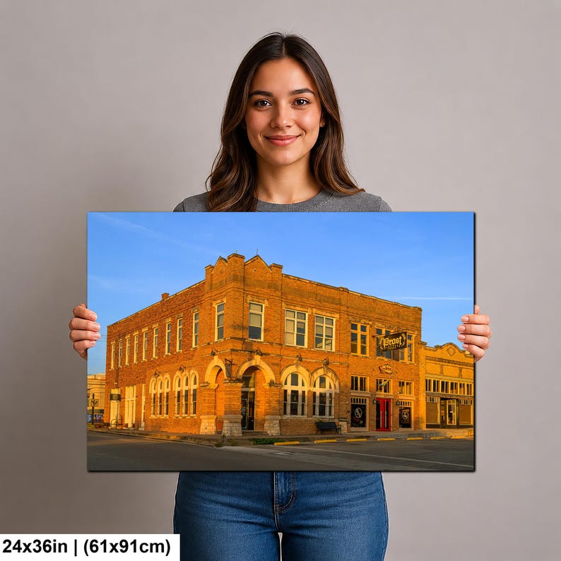 May include: A rectangular wall art print measuring 24 by 36 inches, featuring a photograph of a multi-story orange brick building with arched windows and a sign reading Depot. The structure is set against a clear blue sky during golden hour.