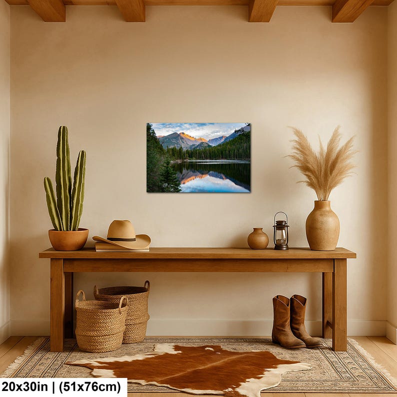 May include: A rectangular wall art print measuring 20 by 30 inches, featuring a landscape photograph of a calm lake reflecting snow-capped mountains at sunrise, surrounded by a dense forest of green pine trees under a soft blue and orange sky.
