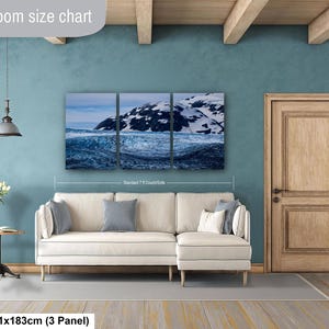 May include: A three-panel wall art set depicting a snowy mountain landscape above a dark blue ocean, displayed above a cream-colored sectional sofa. The text "Livingroom size chart" and "36x72in | 91x183cm (3 Panel)" is visible on the image.