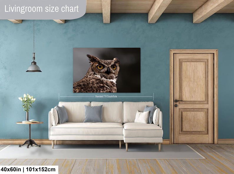 May include: A rectangular wall art print featuring a detailed close-up of a brown and white great horned owl with piercing yellow eyes. The print is displayed above a cream-colored sectional sofa, with text indicating a 40x60 inch size.