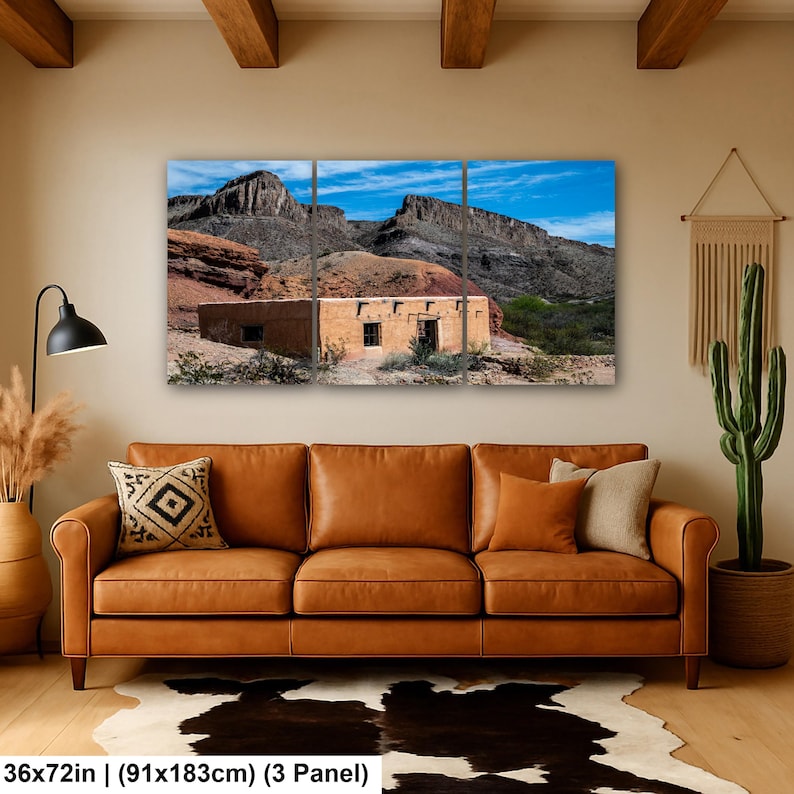 May include: A three-panel wall art set depicting a desert landscape with a tan adobe building nestled against rugged, dark rocky mountains under a bright blue sky. The text at the bottom reads 36x72in (91x183cm) (3 Panel).
