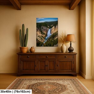 May include: A rectangular wall art print measuring 30 by 40 inches, depicting a waterfall cascading through a deep canyon surrounded by dense green pine forests under a blue sky. The artwork is displayed in a room with a wooden sideboard.