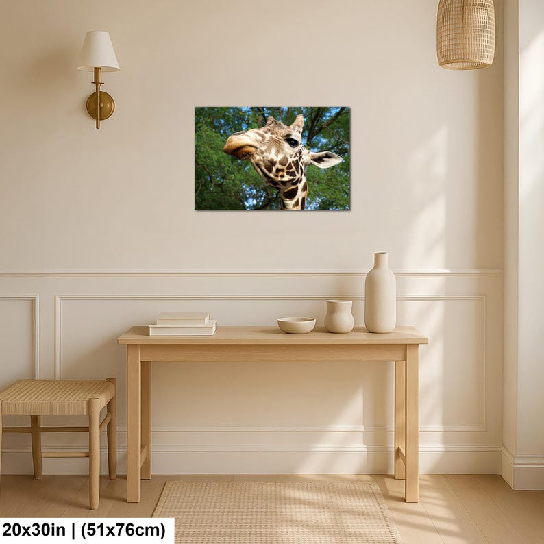 K&ouml;nnte beinhalten: Ein rechteckiger Wandkunstdruck mit einer Nahaufnahme eines Giraffenkopfes vor einem Hintergrund aus gr&uuml;nen B&auml;umen und blauem Himmel. Der Druck misst 51 cm mal 76 cm und h&auml;ngt an einer hellen Wand &uuml;ber einem h&ouml;lzernen Konsolentisch.