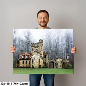Op de afbeelding: Een rechthoekige wandkunstprint met een stenen kasteel met een roodbruin dak, tegen een achtergrond van hoge, bladloze bomen in een mistig bos. De print meet 76 bij 102 cm en toont een groen gazon op de voorgrond.