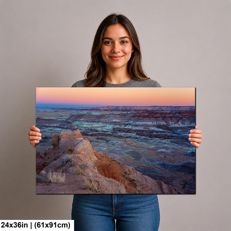 May include: A rectangular wall art print measuring 24 by 36 inches, featuring a landscape photograph of a desert canyon at sunset. The image displays layered rock formations in shades of orange, blue, and grey under a soft pink and orange sky.