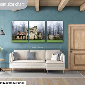 Op de afbeelding: Een driedelige canvas wandkunstset met een stenen kasteel in een mistig bos, weergegeven boven een cr&egrave;mekleurige hoekbank. De tekst Livingroom size chart en 40x90in | 101x229cm (3 Panel) is zichtbaar in de afbeelding.