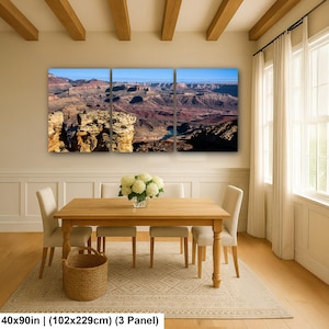 May include: A three-panel wall art set depicting a panoramic view of the Grand Canyon with layered rock formations, a winding river, and a clear blue sky. The artwork measures 40 by 90 inches in total, featuring deep red, brown, and blue tones.