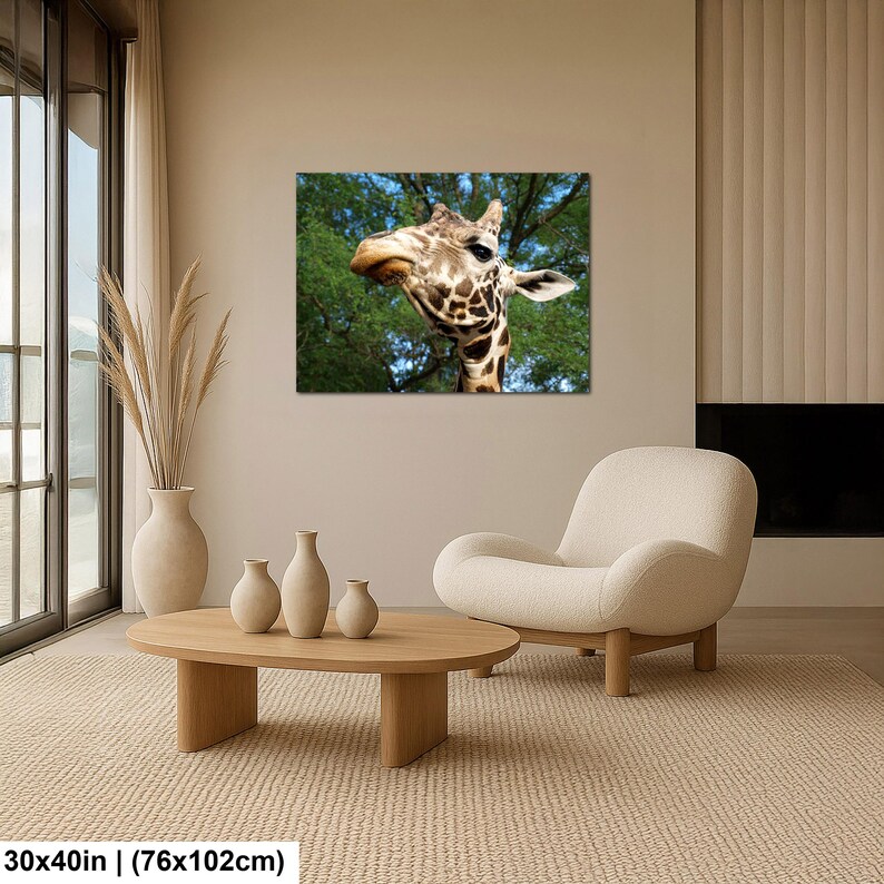 K&ouml;nnte beinhalten: Ein rechteckiger Wandkunstdruck, der den Kopf und Hals einer Giraffe vor einem Hintergrund aus gr&uuml;nen B&auml;umen und blauem Himmel zeigt. Der Druck misst 76 mal 102 cm und h&auml;ngt an einer beigen Wand &uuml;ber einem h&ouml;lzernen Couchtisch und einem cremefarbenen Sessel.