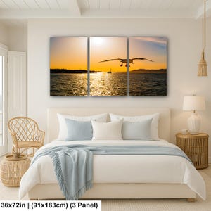 May include: A three-panel wall art set depicting a seagull in flight over a body of water during a golden sunset. The scene features a bright orange sky, a distant shoreline, and shimmering reflections on the water. The total size is 36x72 inches.