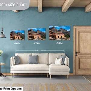 May include: A living room size chart displaying three landscape-oriented wall art prints of a desert adobe structure. The prints are labeled with dimensions of 16x24 inches, 20x30 inches, and 24x36 inches, shown hanging above a cream-colored sectional sofa.