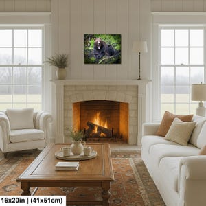 May include: A rectangular wall art print featuring a brown bear resting in a lush green forest setting. The artwork is displayed above a fireplace and measures 16 inches by 20 inches, as indicated by the text at the bottom of the image.