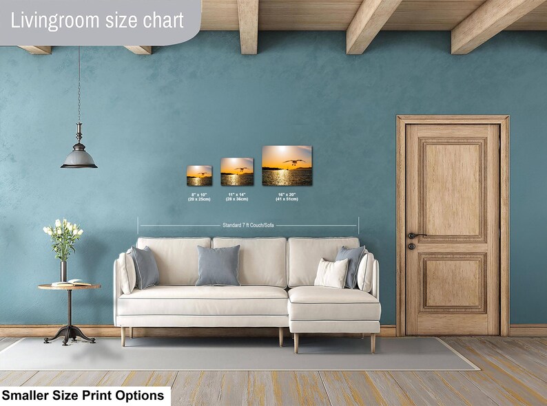 May include: A living room size chart displaying three rectangular wall art prints featuring a sunset over water with a bird in flight. The prints are labeled with dimensions of 8x10 inches, 11x14 inches, and 16x20 inches above a white sofa.