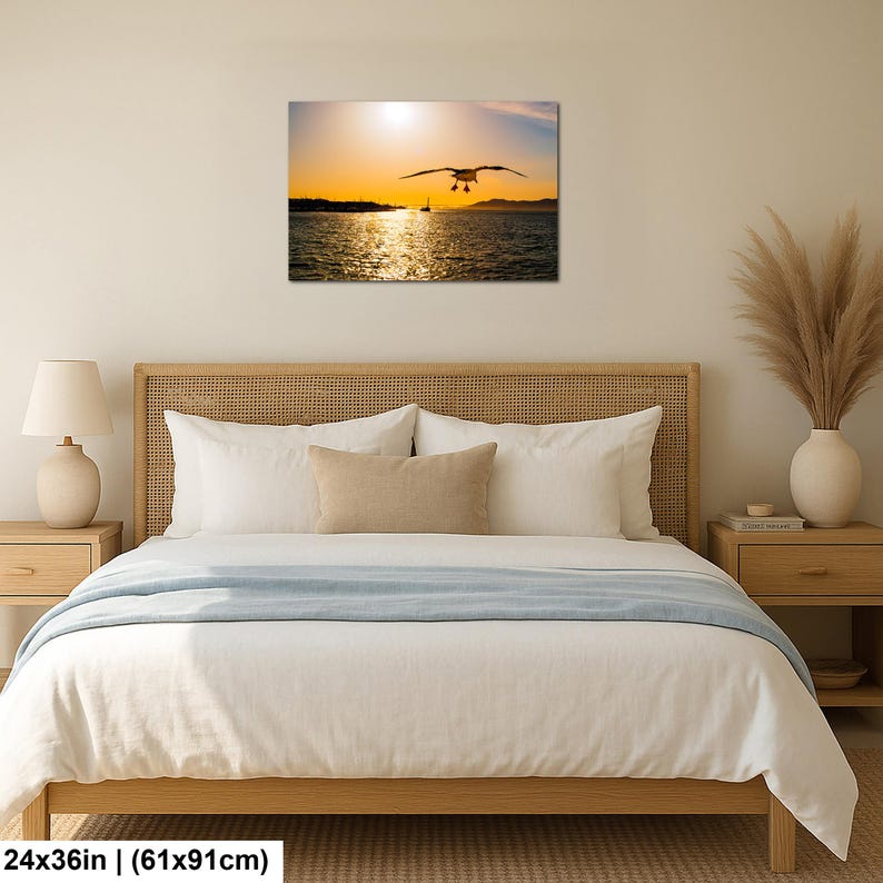 May include: A rectangular wall art print featuring a seagull in flight over a body of water during a golden sunset. The scene includes a distant shoreline and a small boat silhouette under a bright sun, measuring 24 inches by 36 inches.