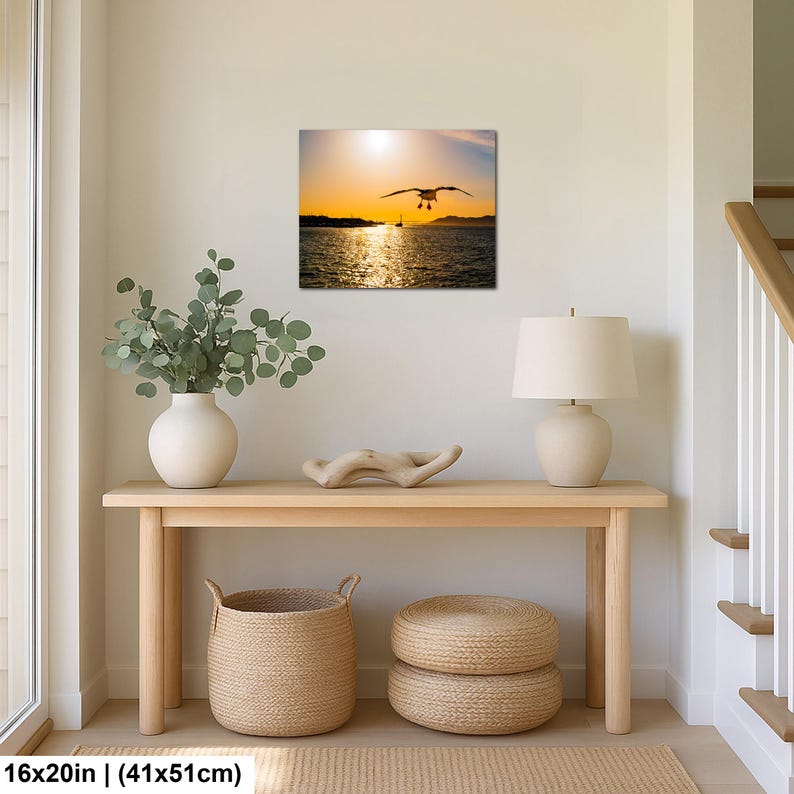 May include: A rectangular wall art print featuring a seagull in flight over a sunlit ocean at sunset. The scene includes a distant shoreline and a small boat silhouette under a bright golden sky, measuring 16 inches by 20 inches in total size.