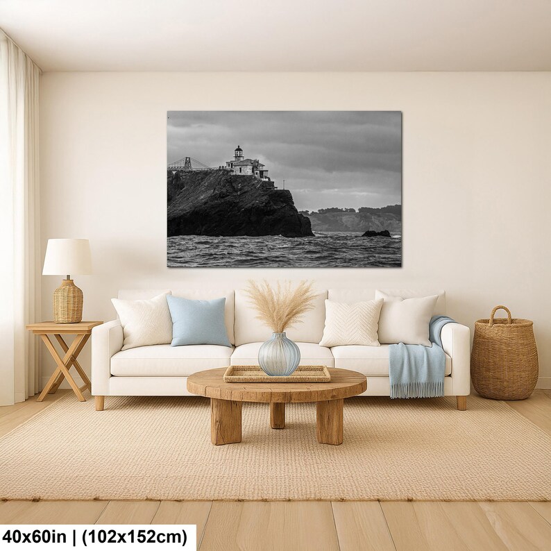 May include: A black and white landscape wall art print featuring a lighthouse perched on a rocky cliff overlooking the ocean under a cloudy sky. The rectangular artwork measures 40 inches by 60 inches and is displayed above a white sofa.