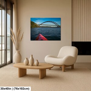 May include: A rectangular wall art print featuring a landscape photograph of a red kayak bow on dark blue water, facing a large arched bridge under a bright blue sky. The print dimensions are clearly labeled as 30 inches by 40 inches.