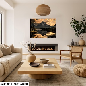 Puede incluir: Un cuadro rectangular de pared que mide 76 por 102 cm, con una fotograf&iacute;a de paisaje de una cordillera reflejada en un lago tranquilo al atardecer con nubes doradas, exhibido sobre una chimenea en un entorno de sala de estar.