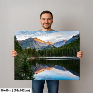 May include: A rectangular wall art print measuring 30x40 inches featuring a landscape photograph of a calm lake reflecting snow-capped mountain peaks at sunrise, surrounded by a dense forest of dark green pine trees under a cloudy sky.