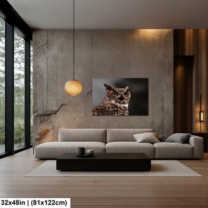May include: A rectangular wall art print featuring a detailed close-up of a great horned owl with piercing yellow eyes and brown mottled feathers. The artwork measures 32 inches by 48 inches and is displayed above a long, low-profile sofa.