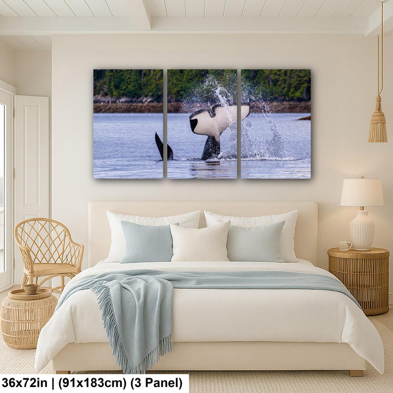 May include: A three-panel wall art set depicting an orca whale tail breaching the water surface, creating a large splash. The scene features the black and white tail against a blue ocean and a green forested shoreline. Measures 36 by 72 inches.