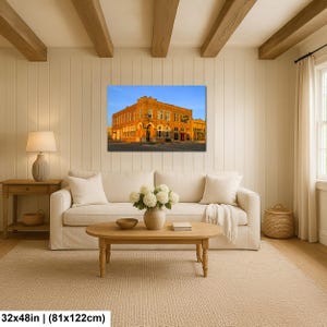 May include: A rectangular wall art print featuring a historic orange brick building under a clear blue sky, displayed in a living room setting with a white sofa, wooden coffee table, and a lamp. The print measures 32 inches by 122 inches.