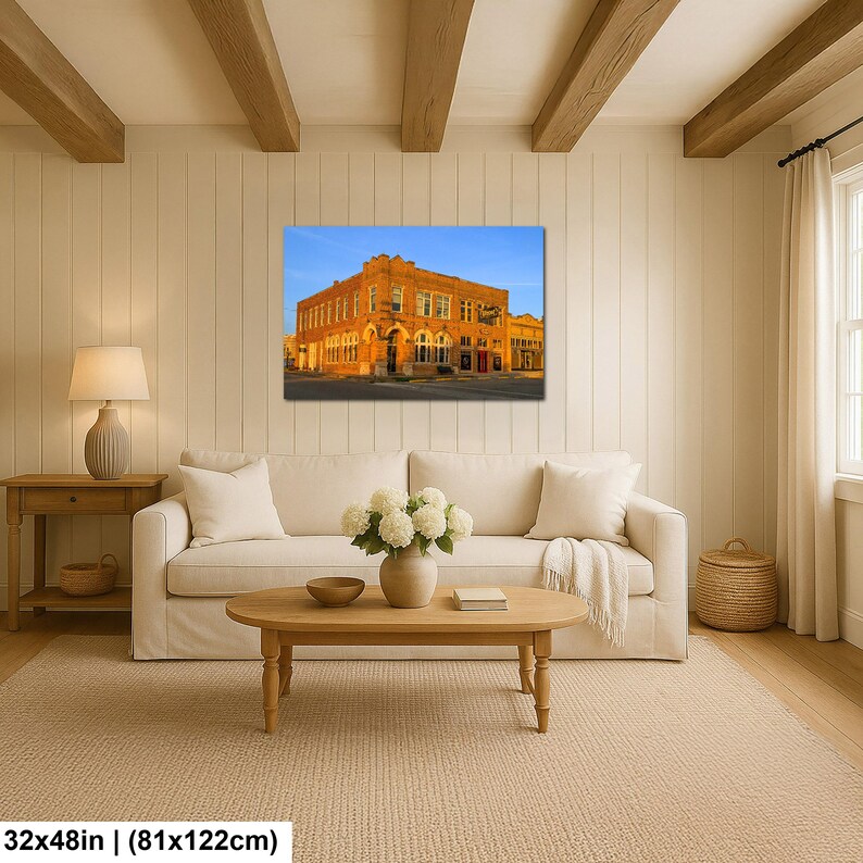 May include: A rectangular wall art print featuring a historic orange brick building under a clear blue sky, displayed in a living room setting with a white sofa, wooden coffee table, and a lamp. The print measures 32 inches by 122 inches.