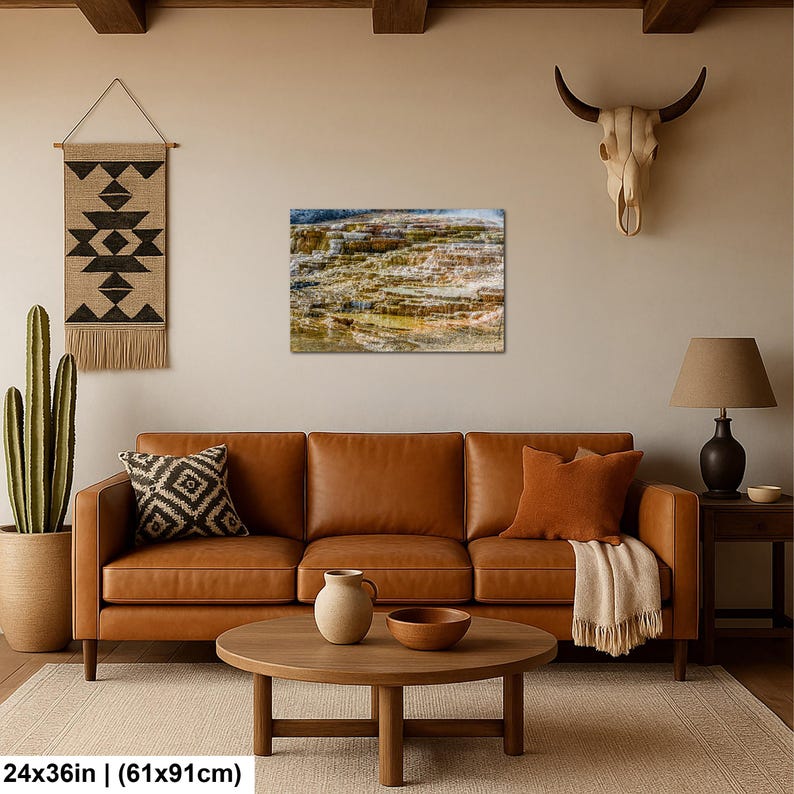May include: A rectangular wall art print featuring a landscape of layered mineral terraces in shades of orange, brown, and white. The print measures 24 inches by 36 inches and is displayed on a wall above a brown leather sofa and coffee table.