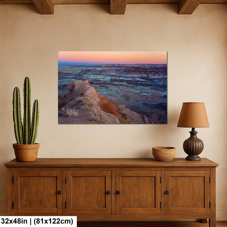 May include: A rectangular wall art print measuring 32 by 48 inches, displaying a desert landscape at sunset with layered rock formations in shades of orange, blue, and purple under a gradient sky transitioning from pink to deep blue.