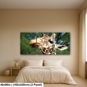 K&ouml;nnte beinhalten: Ein dreiteiliges Wandbild-Set mit einer Nahaufnahme eines Giraffenkopfes mit braunen Flecken vor einem gr&uuml;nen Laub-Hintergrund. Das Kunstwerk misst insgesamt 102 mal 229 cm und zeigt das Gesicht des Tieres, dunkle Augen und die gemusterte Haut.