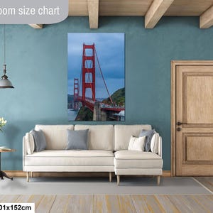 May include: A vertical wall art print of the Golden Gate Bridge in red, displayed above a cream-colored sectional sofa. The print measures 40x60 inches. The scene features the bridge against a cloudy sky, with green hills and water visible below.