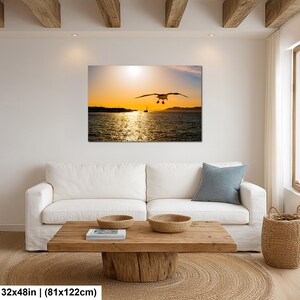 May include: A rectangular wall art print featuring a seagull in flight over a dark ocean at sunset. The golden sun hangs low on the horizon, casting a bright reflection across the rippling water. The print measures 32 inches by 48 inches.