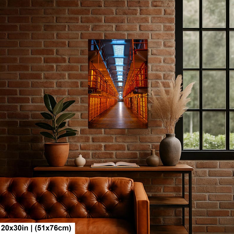 May include: A rectangular wall art print measuring 20 by 30 inches, featuring a perspective view of a multi-level prison cell block with orange metal railings and stairs, illuminated by a bright blue light source from the ceiling skylight.
