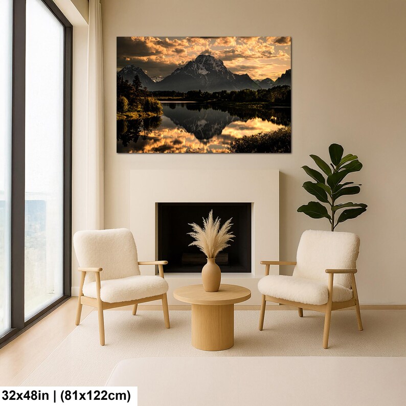 Puede incluir: Un cuadro rectangular que muestra un paisaje de monta&ntilde;a al atardecer con nubes doradas reflejadas en un lago tranquilo. La impresi&oacute;n mide 81 por 122 cm y se exhibe sobre una chimenea entre dos sillones de color crema y una planta.