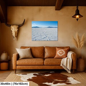 May include: A rectangular wall art print measuring 30 by 40 inches, featuring a landscape of the Bonneville Salt Flats with a cracked white salt crust, distant blue mountains, and a clear blue sky, displayed above a brown leather sofa.