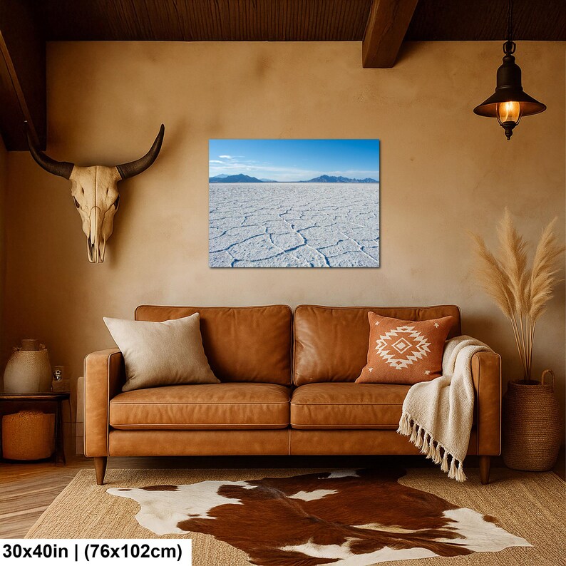 May include: A rectangular wall art print measuring 30 by 40 inches, featuring a landscape of the Bonneville Salt Flats with a cracked white salt crust, distant blue mountains, and a clear blue sky, displayed above a brown leather sofa.