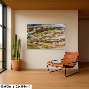 May include: A rectangular wall art print featuring a landscape of layered mineral terraces with flowing water in shades of brown, orange, and white. The print measures 40x60 inches and is displayed on a plain wall next to a cactus and a leather chair.