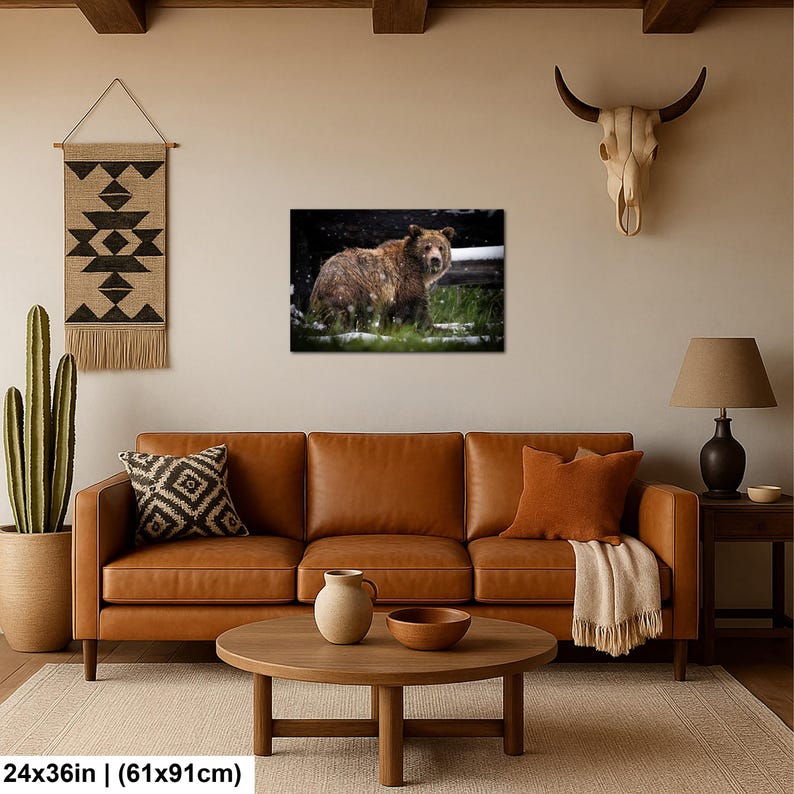 May include: A rectangular wall art print measuring 61 by 91 cm, featuring a brown bear standing in a snowy, grassy landscape. The bear is captured in profile, looking toward the viewer amidst light snowfall and dark, blurred background foliage.
