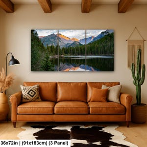 May include: A three-panel wall art set depicting a mountain lake landscape with pine trees and snow-capped peaks at sunrise. The artwork measures 36 by 72 inches in total. The scene features a calm lake reflecting the mountains and forest.