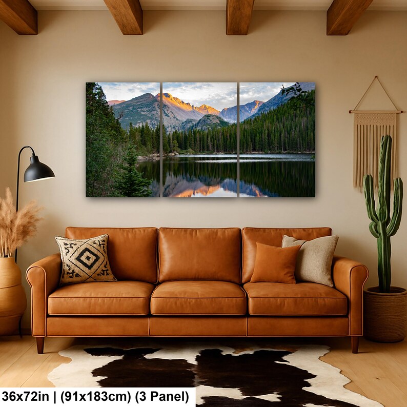 May include: A three-panel wall art set depicting a mountain lake landscape with pine trees and snow-capped peaks at sunrise. The artwork measures 36 by 72 inches in total. The scene features a calm lake reflecting the mountains and forest.