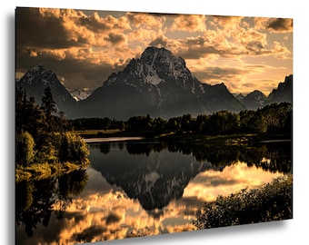 May include: A rectangular wall art print featuring a landscape of a snow-capped mountain peak reflecting in a calm lake at sunset. The sky is filled with golden-hued clouds, and dark silhouettes of trees line the shore in the foreground.